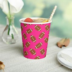 a pink paper cup with footballs and strawberries on it, next to a white flower