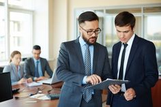 two men in suits looking at something on a clipboard