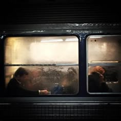 two people sitting on a train looking out the window at something in the distance,