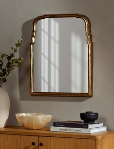 a wooden dresser topped with a mirror next to a vase filled with flowers and books