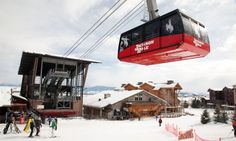 a ski lift with people on it above the snow covered ground and buildings in the background