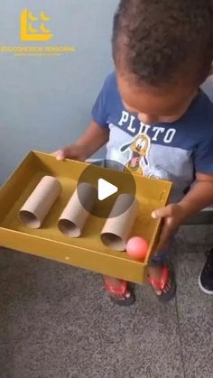 a little boy is playing with some toilet paper rolls in a cardboard box on the floor