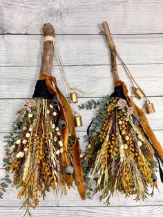 two dried flowers and leaves hang from twine on a white wooden background with bells