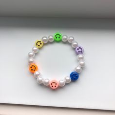 a bracelet with different colored smiley faces and white pearls on the front, along with an additional bead