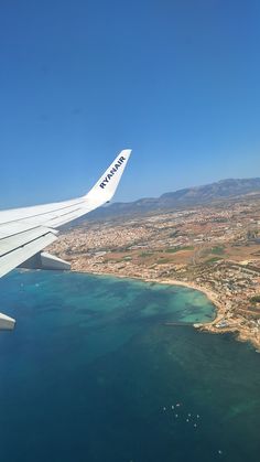 the wing of an airplane flying over a city next to the ocean and beach area