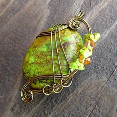 a wire wrapped pendant with green and yellow beads on it's end, sitting on a wooden surface