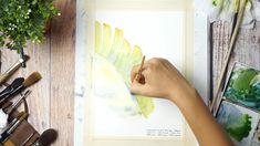 a person is holding a paintbrush and painting leaves on a piece of paper with watercolors