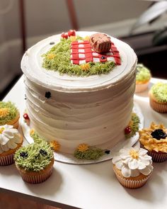 cupcakes are arranged around a white cake with green frosting and decorations on it