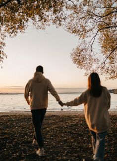 a man and woman holding hands walking on the beach with trees in front of them