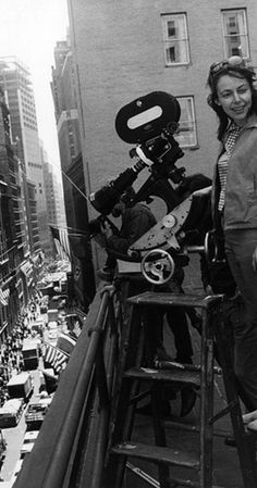 a woman standing on top of a ladder next to a camera set up in the city