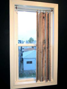 an open window with wooden slats in front of it and a white house behind