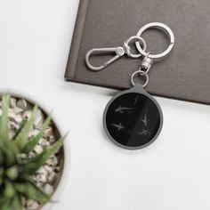 a black keychain with birds on it sitting next to a potted plant