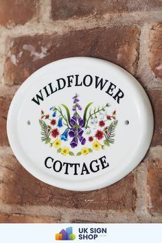 a white sign that says wildflower cottage hanging on the side of a brick wall