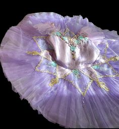 a purple tutu with gold trim and beads on it's bottom, sitting in front of a black background