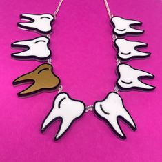 Tooth 🦷 fairy necklace is a fun, quirky accessory to pair with a any outfit. The necklace is made from white, gold and black gloss acrylic layered on a clear background. The teeth are linked together using jump rings and is linked to a curb chain with a lobster claw clasp.  Just leave a note 📝 at checkout with the word or name you would like made. If you have any questions drop us a line!💌 We are more than happy to help😁 To clean your necklace you can simply wipe with a glasses cloth or soft cloth to remove finger marks. Acrylic is a fragile material so please store in a jewellery box to prevent damage.  As ever for safety please keep away from small children. Novelty White Handmade Necklace, Handmade White Novelty Necklace, Plastic Jewellery, Laser Cut Jewelry, Fairy Necklace, Clear Background, Black Gloss, The Teeth, Statement Jewellery