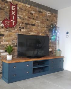 a flat screen tv sitting on top of a blue entertainment center next to a brick wall