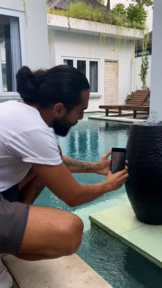 a man sitting on the edge of a swimming pool while looking at his cell phone