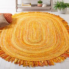 a yellow rug with fringes on the floor in front of a shelf and potted plant