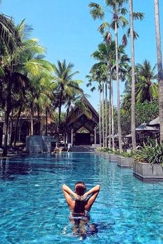 a woman standing in the middle of a pool surrounded by palm trees