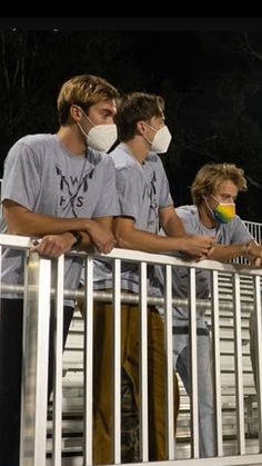 three boys wearing face masks standing on a balcony