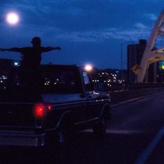 a man standing on the back of a pickup truck in front of a bridge at night