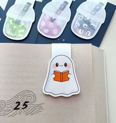 three little ghost bookmarks are sitting on top of a paper bag with buttons in them