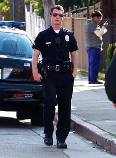 a police officer walking down the street with his hand in his pocket and sunglasses on