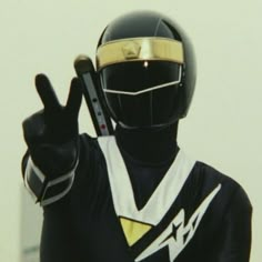 a person in a black and gold uniform holding up a peace sign with both hands