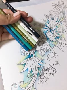 a person holding four colored pencils in their hand next to an open coloring book