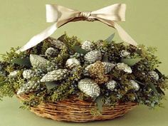 a basket filled with pine cones and greenery next to a white ribbon on a green wall