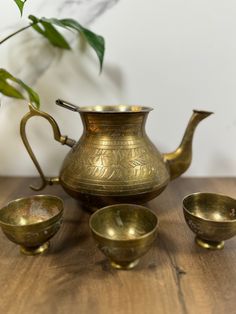 an antique brass tea set on a wooden table next to a potted plant and four small bowls