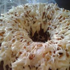 a bundt cake with white frosting and nuts on top sitting in a plastic container