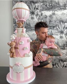 a man holding a baby in front of a pink and white cake with hot air balloons