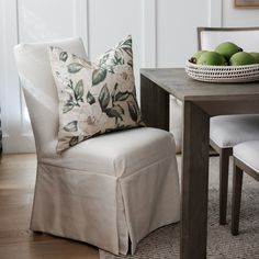 a chair with a flowered pillow on it next to a bowl of green apples