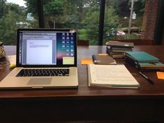 an open laptop computer sitting on top of a wooden desk next to books and notebooks