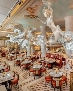 the interior of a fancy restaurant with statues on the walls and tables in red chairs