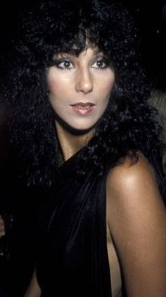 a woman with long black hair wearing a black dress and posing for the camera at an event