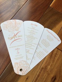 three wedding program cards sitting on top of a wooden floor