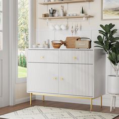 a white dresser sitting in a living room next to a potted plant on top of a rug