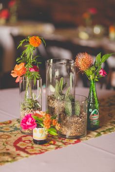 three vases filled with plants and rocks on top of a tablecloth covered table