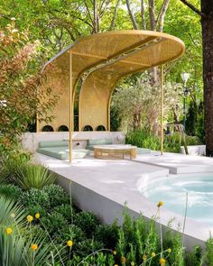 an outdoor swimming pool surrounded by greenery and trees, with a pergolated gazebo in the background