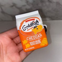 a hand holding an orange and white box shaped like a cheddar with the word goldfish on it