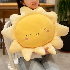 a woman sitting in a chair holding a pillow with a smiling sun on it's face