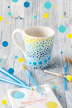 a coffee cup with blue and yellow polka dots on it next to paintbrushes