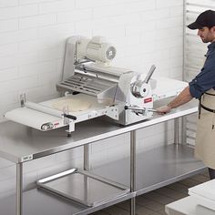 a man standing in front of a machine making pizza