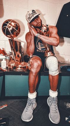 a man sitting on top of a table holding a trophy and basketball trophies in front of him