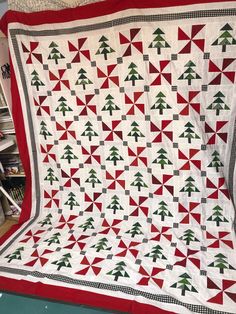 a red and white quilt with christmas trees on it in front of a bookshelf