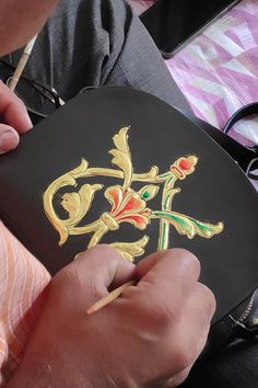 a person is drawing on a piece of black paper with gold lettering and red flowers