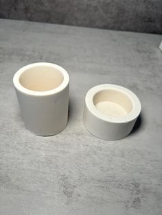 two white vases sitting on top of a gray countertop next to each other