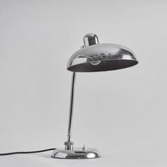 a chrome plated desk lamp with a black cord attached to the base and a white background